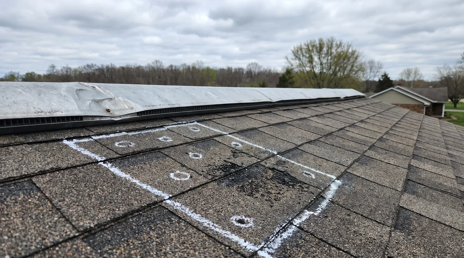 Chalk-marked hail test square on asphalt shingles with a dented ridge vent